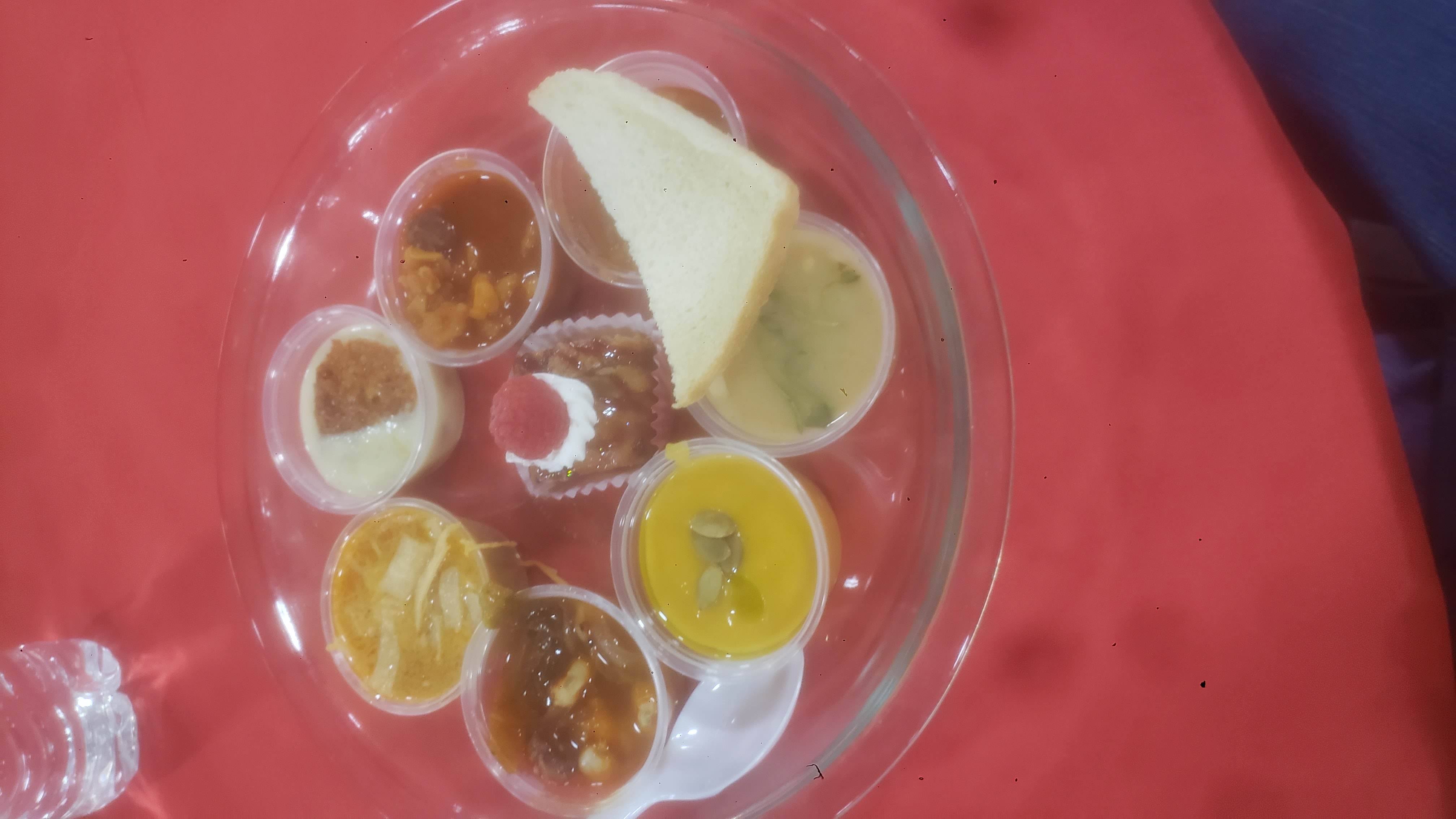 Mini cups of soup and mini desserts in a pie pan with a plastic spoon on a table.